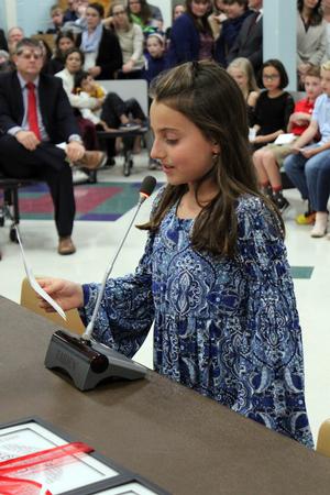 a young girl speaks into a microphone to read a note