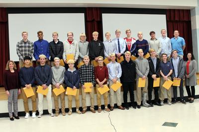 Twenty-eight boys soccer players stand in front of and on a stage holding certificates