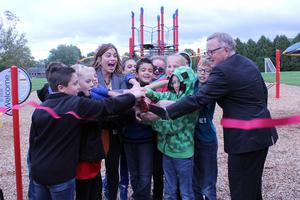 children and two adults cut a red ribbon at a playground