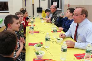 students and adults sit together at a long table eating dinner