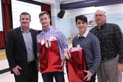 2 men stand with 2 male teenagers who are holding red gift bags