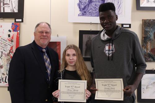 A man stands with a young woman and a young man who are holding certificates