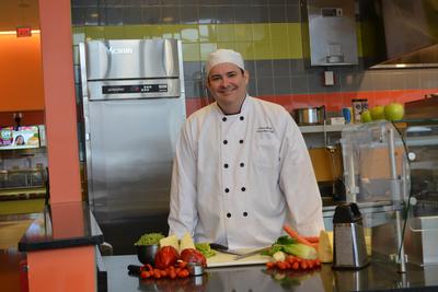 A chef stands in front of a counter that has vegetables on it